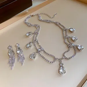 Macro view of crystal water-drop pendant and tassel earrings set on beige tray