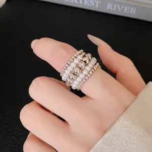 Vista detallada de un elegante anillo multicapa con cuentas plateadas y perlas blancas al dedo