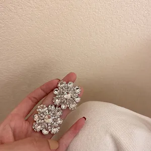 Close-up of sparkling rhinestone flower stud earrings held in hand to show size and detail