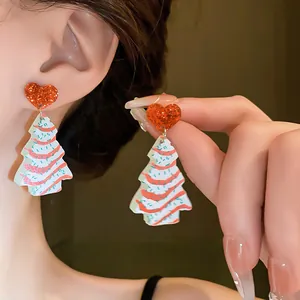 Close-up of festive Christmas tree earrings with red glitter hearts on model's ear.