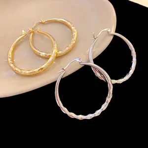 Elegant wave pattern hoop earrings in gold and silver finish on ceramic plate