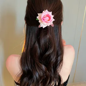 Detail of a sweet pink rose hair clip styled on long wavy dark hair for a romantic look.