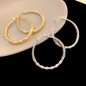 Detailed view of wave-textured metal hoop earrings in gold and silver finishes.