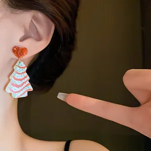 Close-up detail of a Christmas tree earring with a red glitter heart stud on a model's ear.