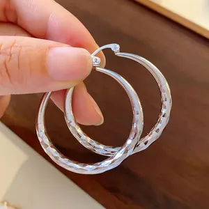 Detail of silver wavy textured hoop earrings held in hand for close-up view.