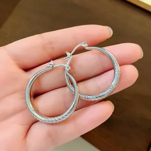 Close-up detail of silver hoop earrings featuring a textured ridge wave pattern held in hand