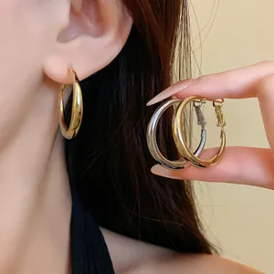 Elegant minimalist gold and silver metallic hoop earrings shown on model's ear and hand