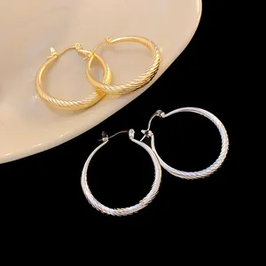 Close-up detail of stylish gold and silver hoop earrings featuring a twisted wave texture