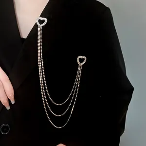Dettaglio di una spilla a cuore con strass e catena a nappe su un blazer nero molto elegante