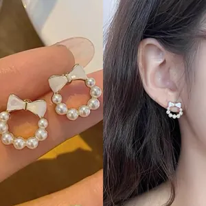 Elegant pearl bow stud earrings shown in a hand-held detail and worn on an ear
