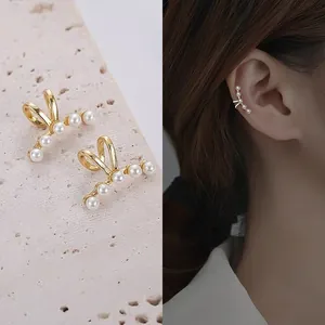 Detail shot of gold-tone pearl crawler earrings with a view of them on a model's ear