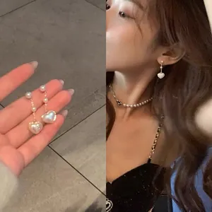 Detailed view of elegant heart-shaped iridescent pearl drop earrings worn by a model