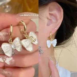 Close-up detail of elegant pearlescent bow drop earrings featuring tiny zircon and gold hoop