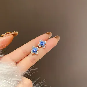 Primo piano di orecchini a lobo a fiore blu Klein con perni in argento su mano