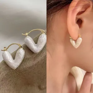 Close-up view of elegant white pearlescent heart-shaped hoop earrings worn on a model's ear