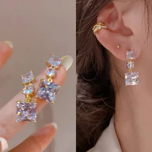Detailed shot of sparkling zircon drop earrings held on finger and worn on a model's ear