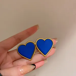 Primo piano di orecchini a cuore blu Klein con bordi dorati tenuti da una mano.