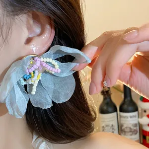 Close-up of light blue chiffon flower earring with colorful glass beads on a model's ear