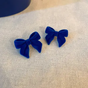 Primo piano di eleganti orecchini a fiocco in velluto blu Klein su tessuto materico