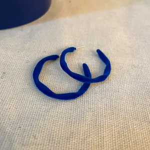 Dettaglio ravvicinato di orecchini a cerchio in velluto blu Klein dal design vintage.