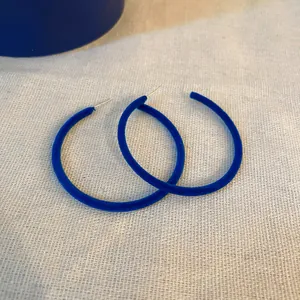 Primo piano di orecchini a cerchio in velluto blu Klein su sfondo beige