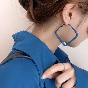Gros plan de boucles d'oreilles carrées bleu Klein sur un modèle