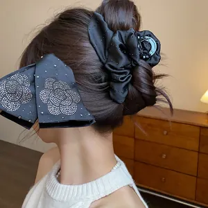 Elegant black fabric hair claw clip featuring a sparkling rhinestone camellia flower design