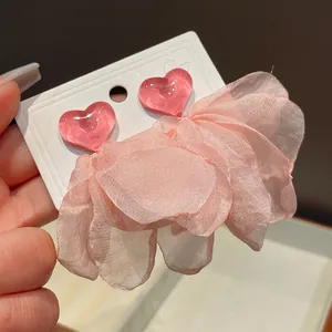 Close-up of pink heart-shaped earrings with large elegant fabric ruffled tassels.