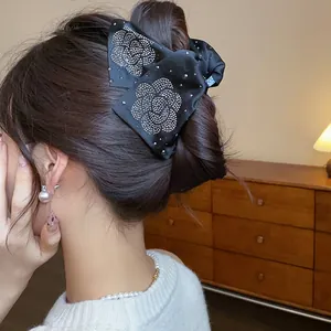 Close-up showing the elegant rhinestone flower design on a black fabric hair claw clip