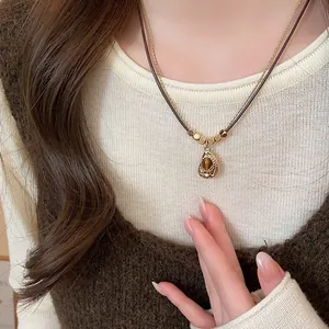 Close-up detail of retro brown tiger eye pendant necklace worn over a beige sweater