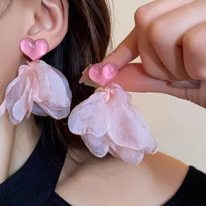 Close-up detail of pink heart earrings with delicate fabric petal tassels on model's ear