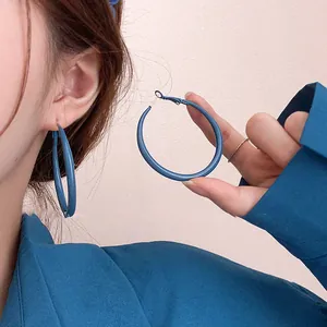 Gros plan de boucles d'oreilles créoles bleu Klein portées et tenues par le modèle