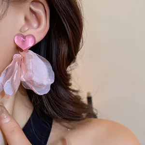 Detail view of pink heart-shaped earrings featuring elegant fabric flower tassels on ear