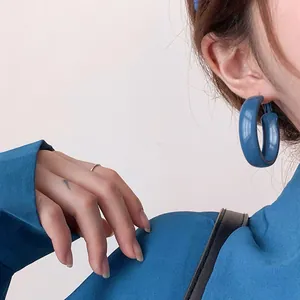 Vue de profil d'un modèle portant des créoles épaisses bleu Klein avec aiguille en argent