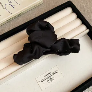Close-up of black fabric hair claw clip with delicate rhinestone embellishments in a tray