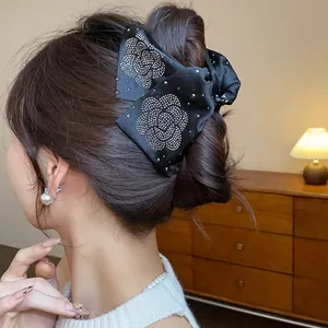 Close-up of black fabric hair claw clip with rhinestone camellia flower patterns