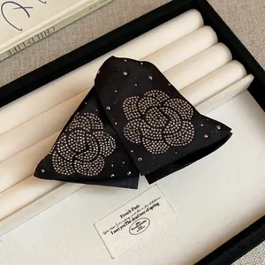 Close-up of elegant black fabric claw clips with rhinestone camellia flower patterns