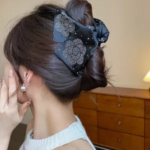 Detailed view of an elegant black fabric bow hair claw clip with sparkling rhinestone flower pattern
