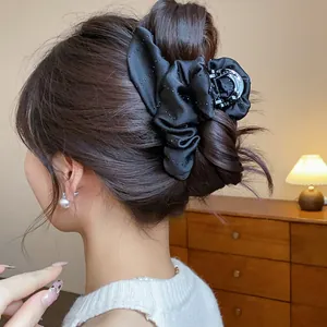 Detail view of a black fabric rhinestone flower hair claw clip on an elegant bun style