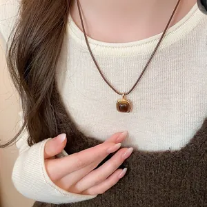 Detail of a retro brown tiger eye stone pendant necklace worn with a white ribbed sweater.