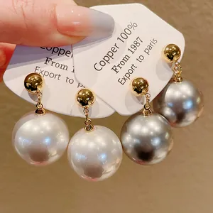 Vue détaillée d'élégantes boucles d'oreilles dorées avec des perles blanches et grises.