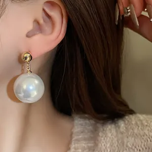 Vue détaillée d'une grande boucle d'oreille en perle blanche avec un clou doré chic