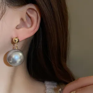 Gros plan d'une grande boucle d'oreille en perle gris argenté avec clou doré sur un modèle