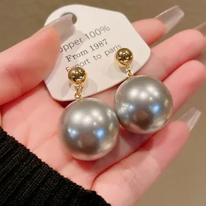 Gros plan sur de grandes boucles d'oreilles perles grises avec placage or