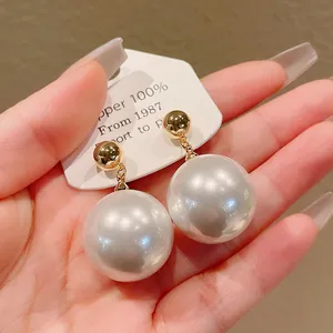 Détail montrant de grandes boucles d'oreilles perles vintage avec des clous dorés en main.