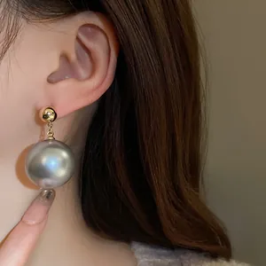 Gros plan d'une élégante boucle d'oreille pendante en perle grise géante sur l'oreille.
