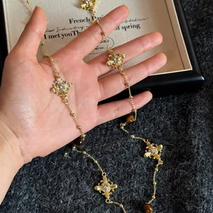Detailed view of a vintage gold cross necklace with tiger eye beads held in hand