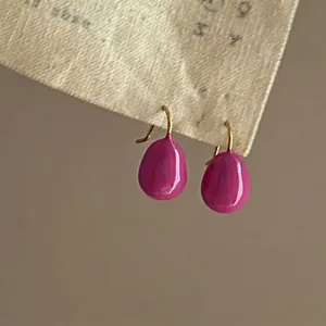Macro shot of fuchsia enamel water drop earrings with gold-plated hooks.
