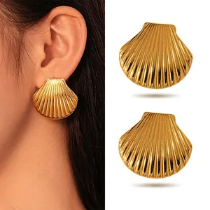 Close-up view of gold seashell earrings with textured surface on white background