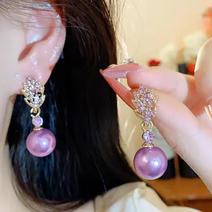 Close-up detail of elegant gold leaf earrings featuring purple crystals and pearls